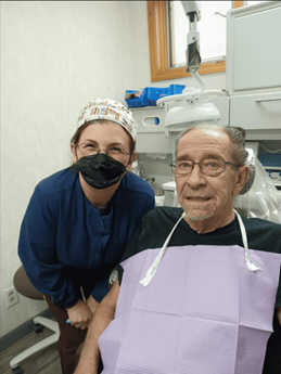 Provider stands behind man in dental chair in a brightly lit clinic setting.